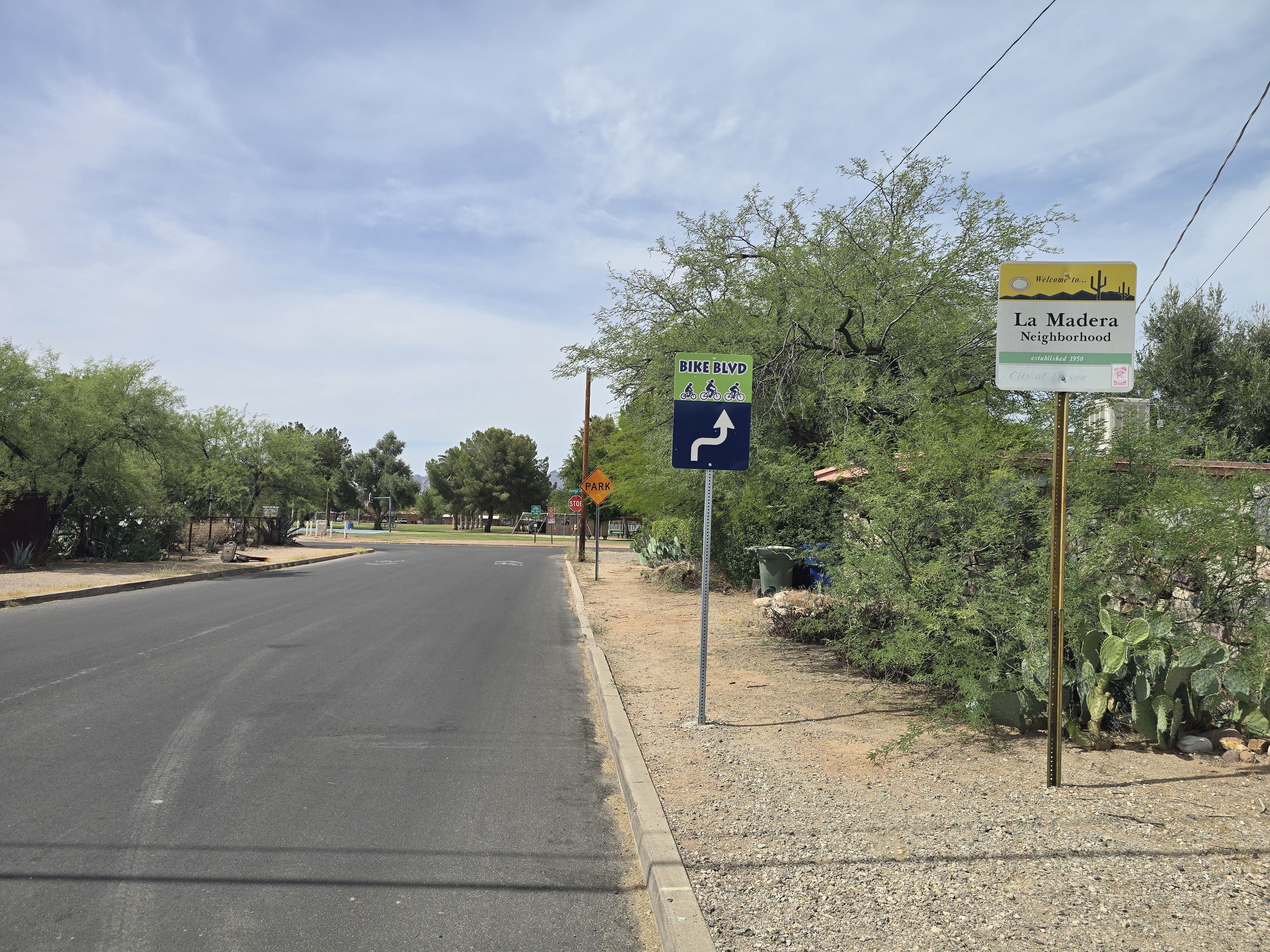 A quiet La Madera street with a green "Bike Blvd" sign and the La Madera Neighborhood welcome sign, desert plants along the curb.