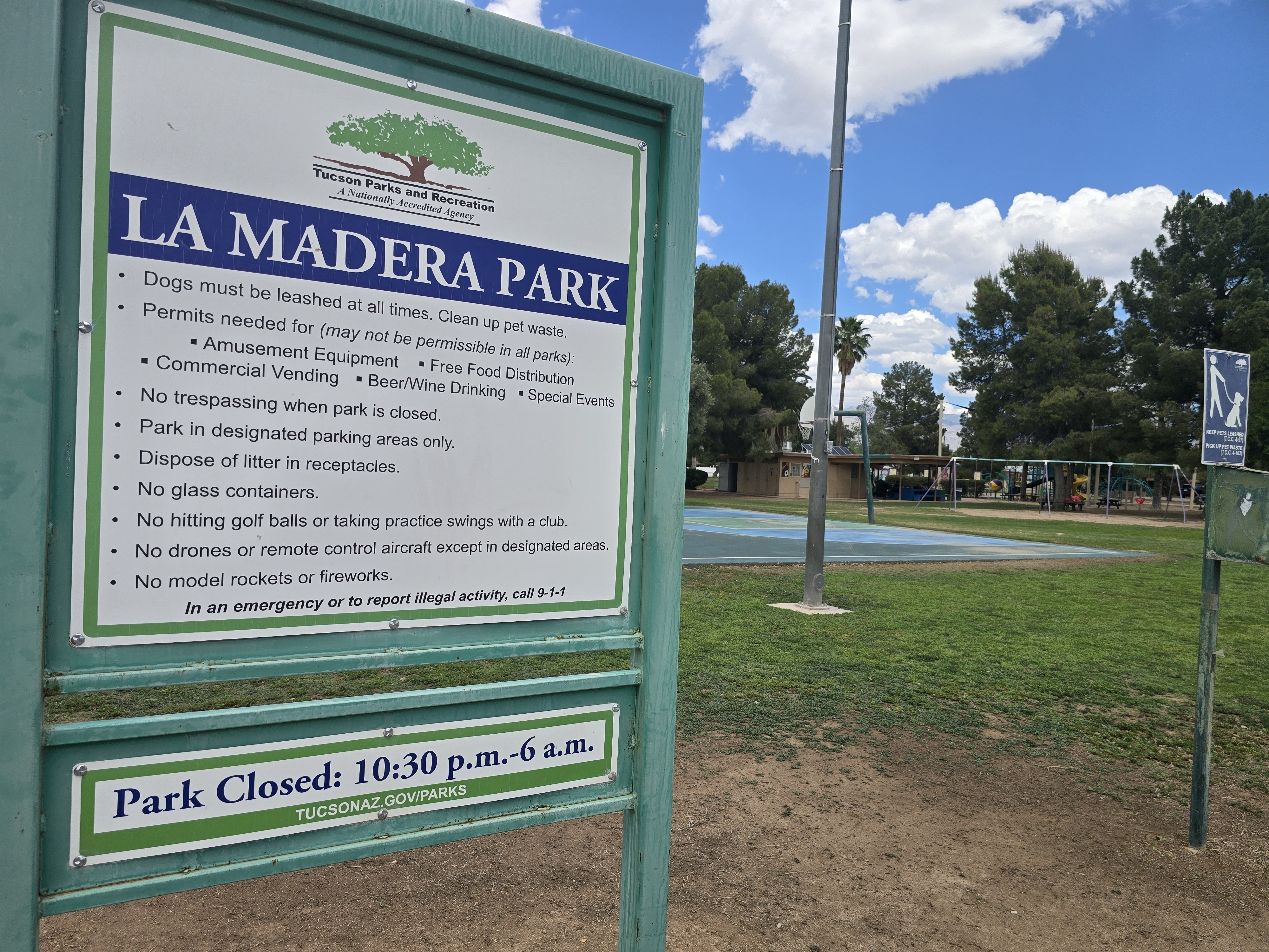 La Madera Park rules sign from Tucson Parks and Recreation, with the basketball court and playground behind it.