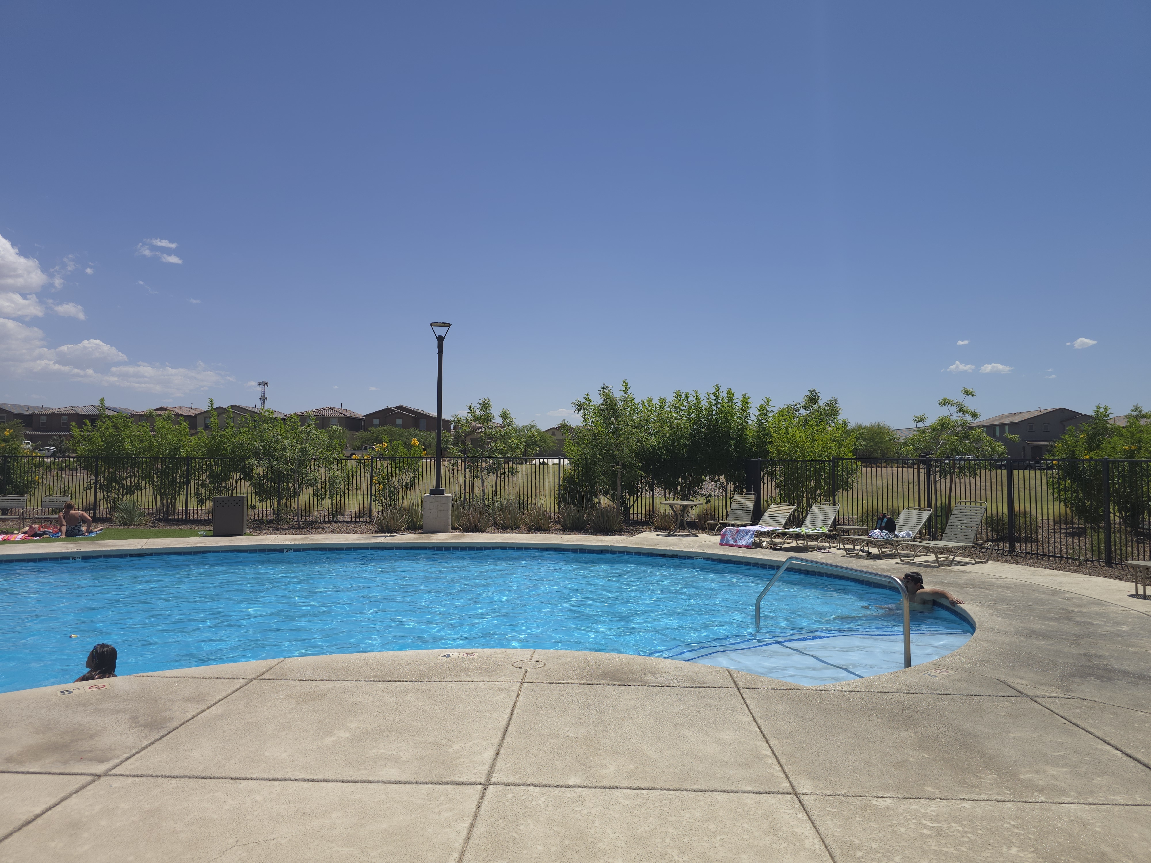 Curved community swimming pool at La Estancia de Tucson with lounge chairs and desert landscaping