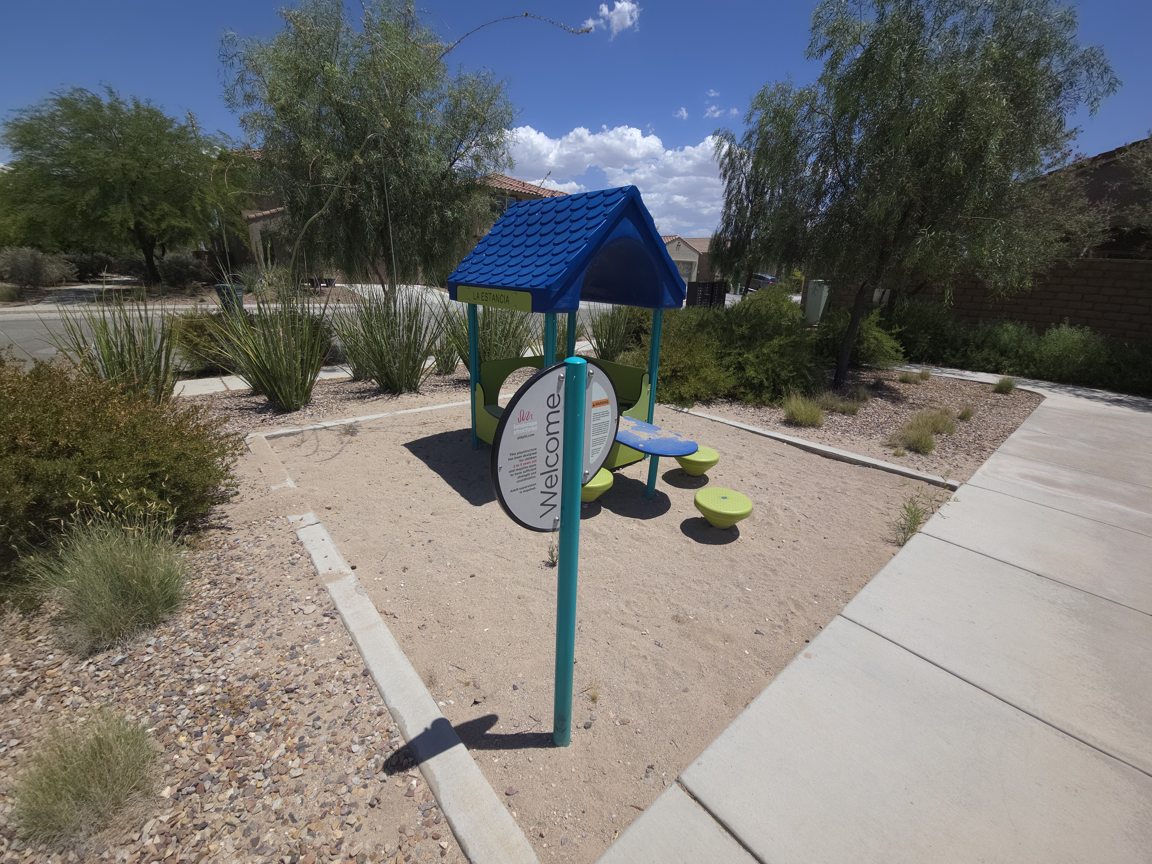 Small toddler-sized play structure with a blue tiled roof at the entrance to a La Estancia neighborhood park