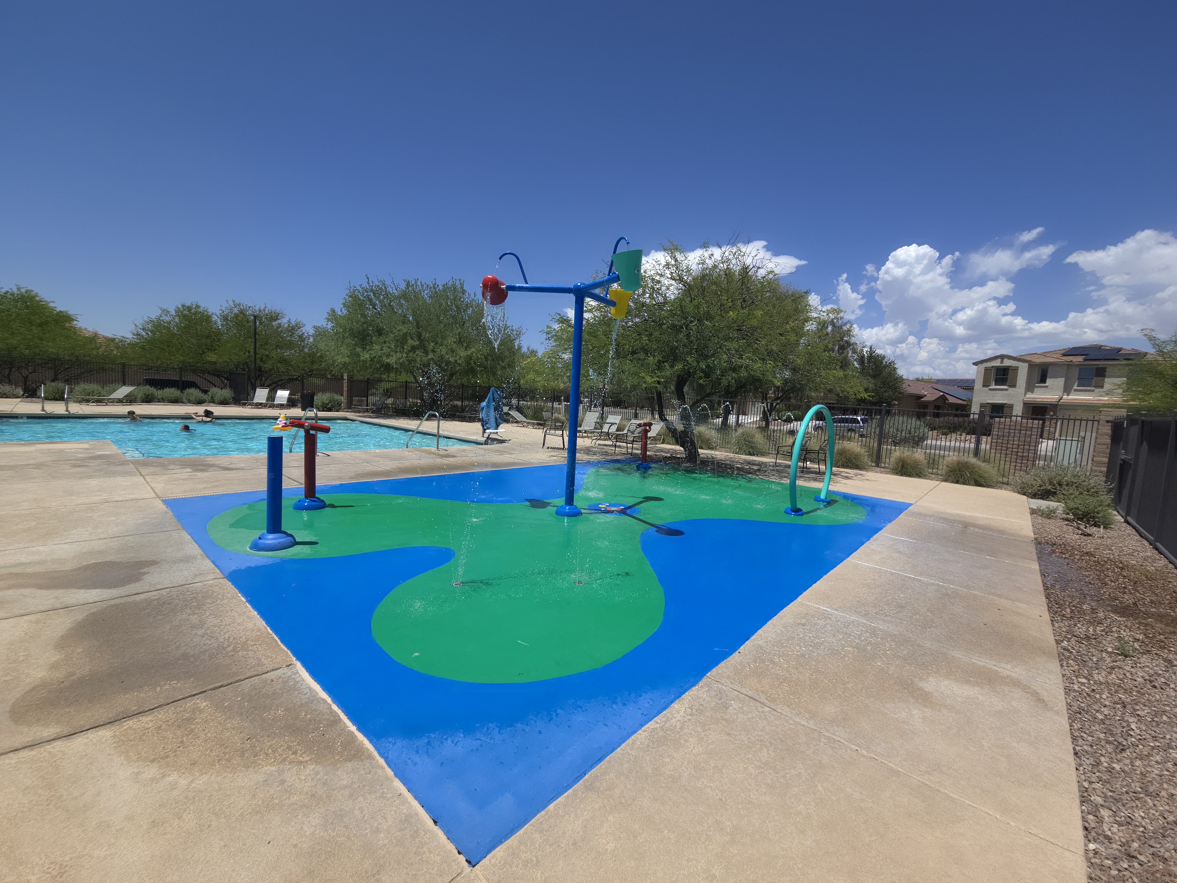 Colorful splash pad with water features and dumping buckets next to the main community pool at La Estancia de Tucson
