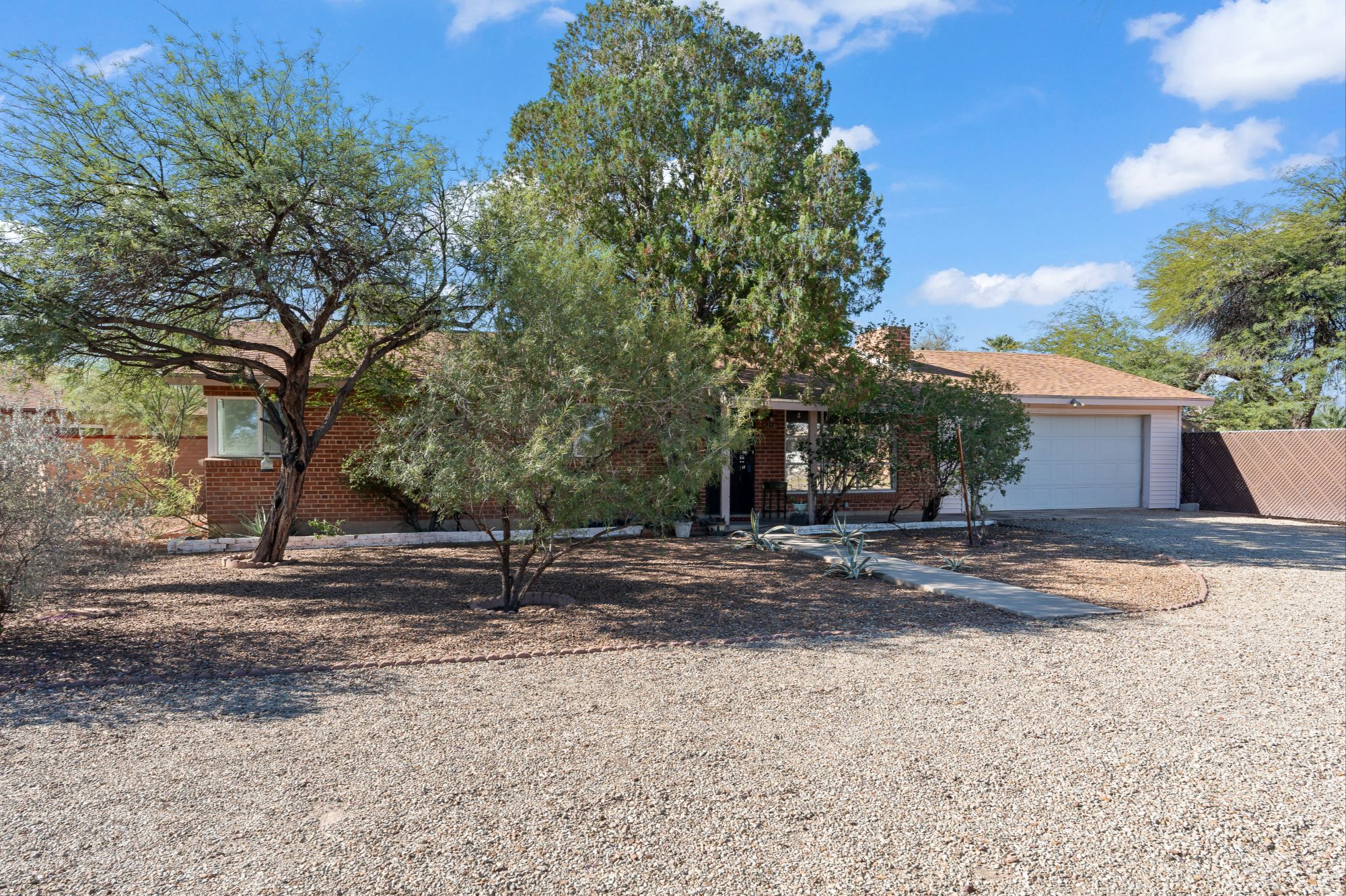 The view from the street toward a front door set far back behind a long gravel driveway