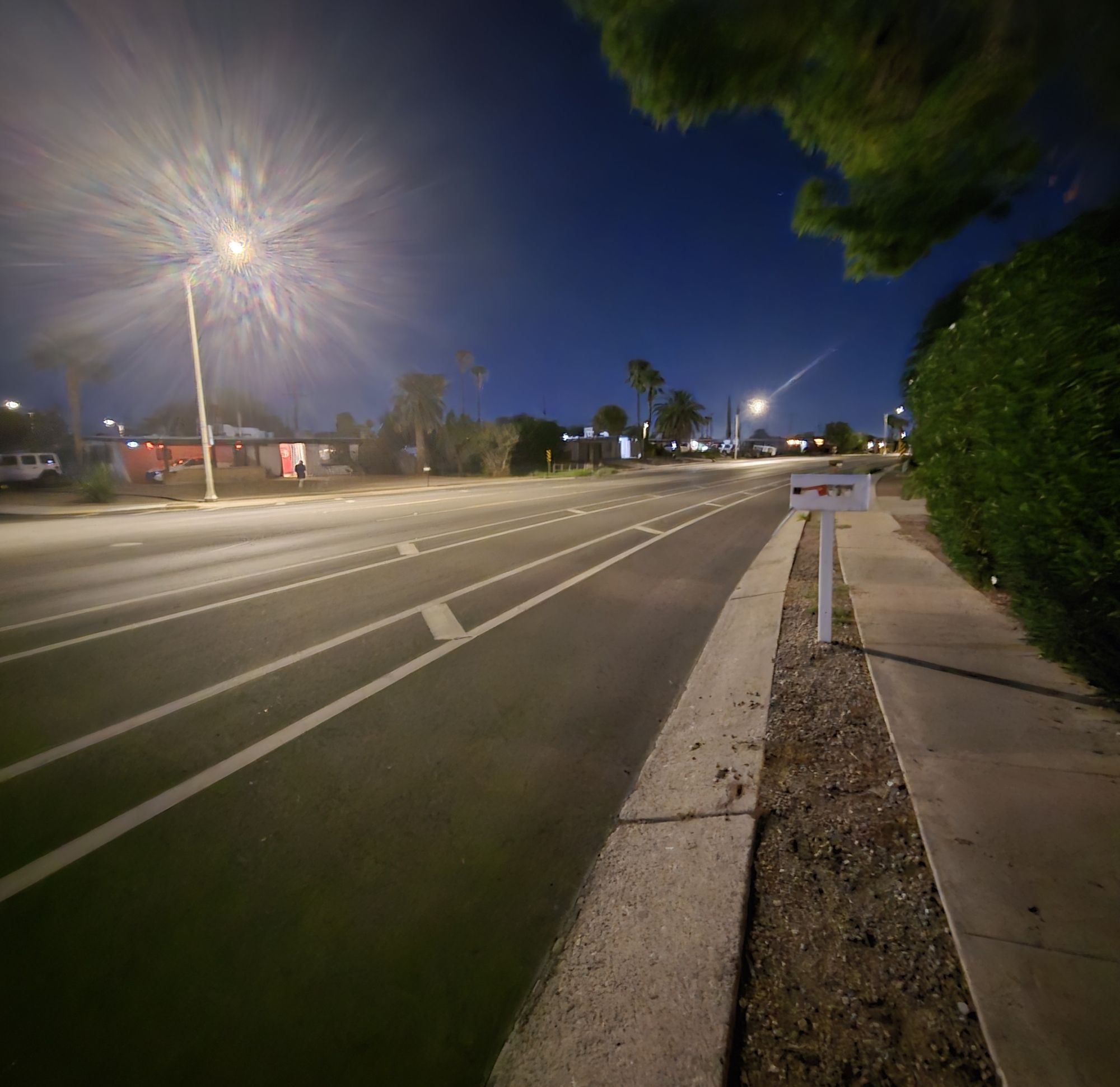 A residential sidewalk at night lit by a working streetlight