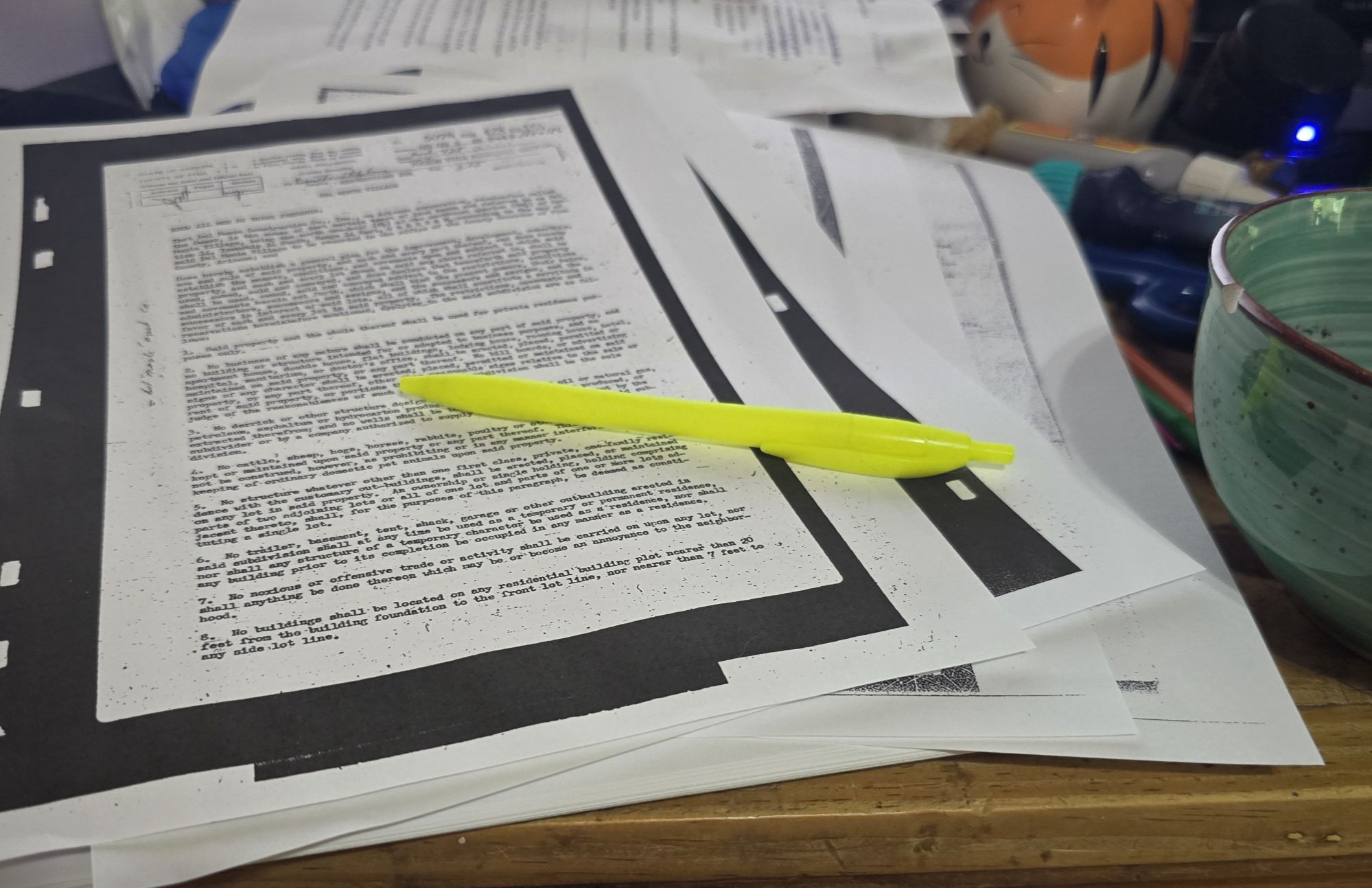 A thick stack of HOA governing documents on a table with a highlighter and bowl