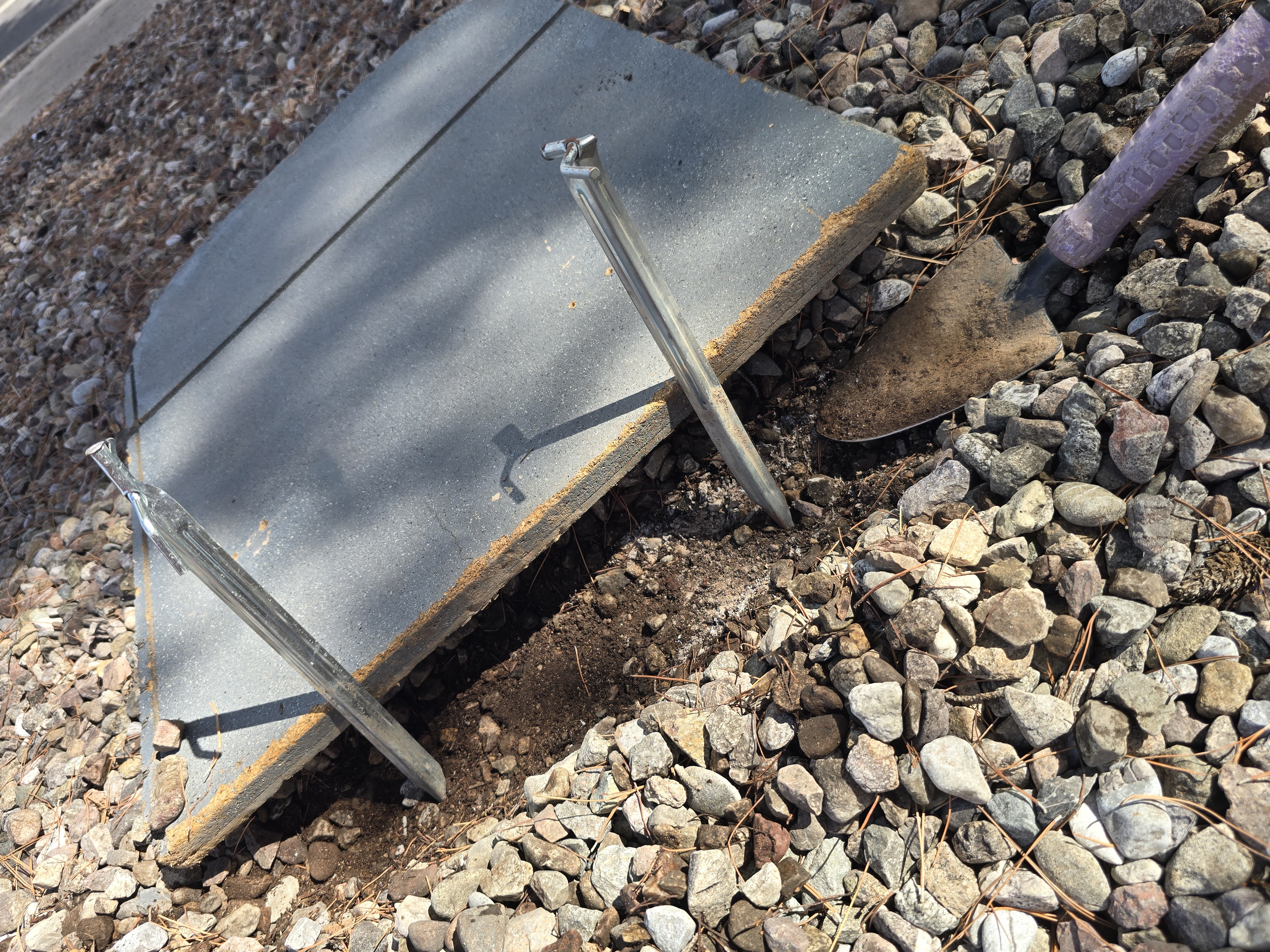Landscape rock cleared aside to expose damp soil, with metal stakes