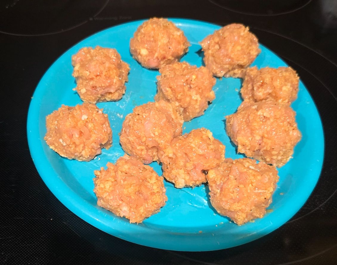 Raw ground chicken meatballs rolled and lined up on a tray