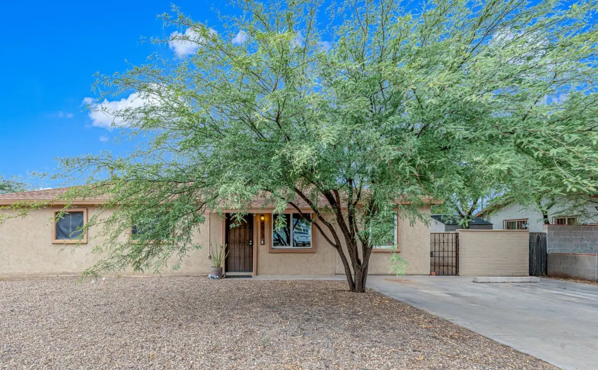 Single-story stucco home with a dark wood door, desert gravel landscaping, and a large mesquite tree shading the front yard.