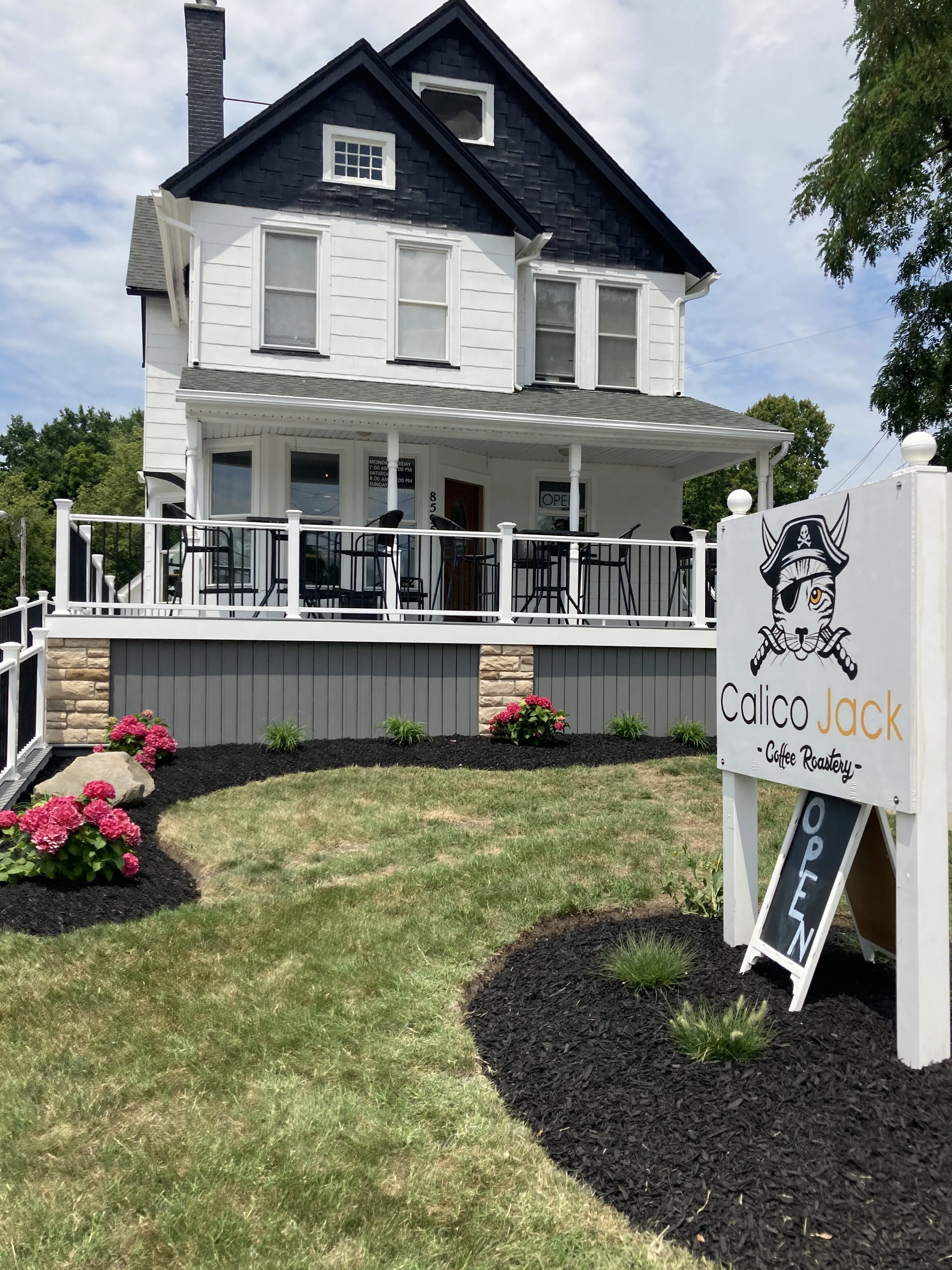 Exterior of Calico Jack Coffee Roastery in Mentor, Ohio, featuring a black-and-white house, front porch and landscaped lawn.