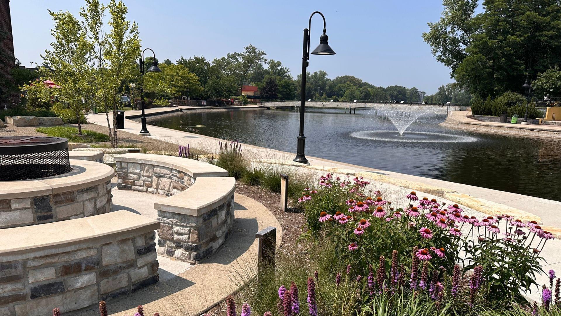 View of the newly renovated Mill Pond and pedestrian walkways in Downtown Brighton, Michigan with fire pit and fountain
