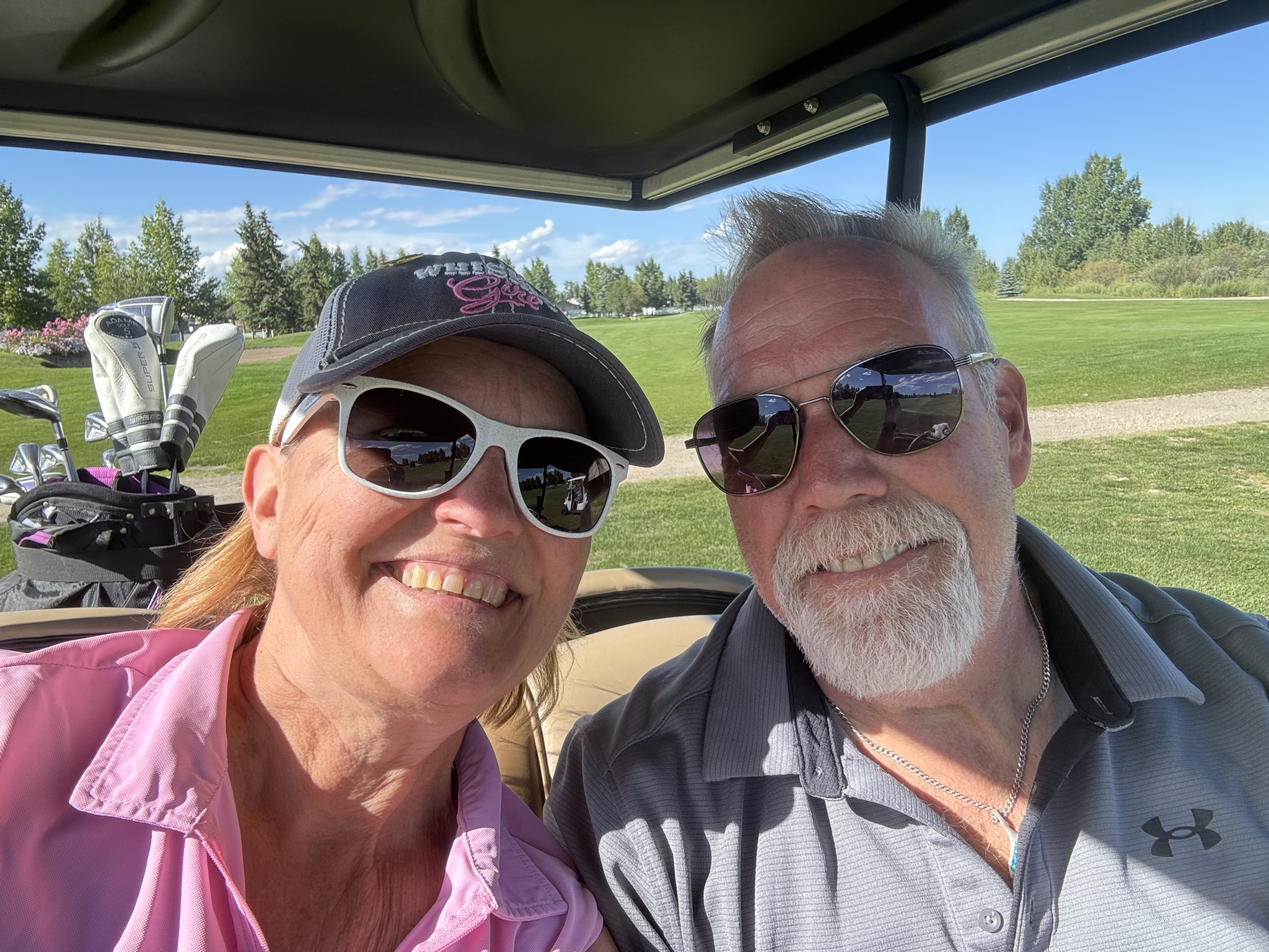 Susan Cramer and Dave Cramer smiling in a golf cart on a sunny day at the Gleniffer Lake Golf Course in Central Alberta.