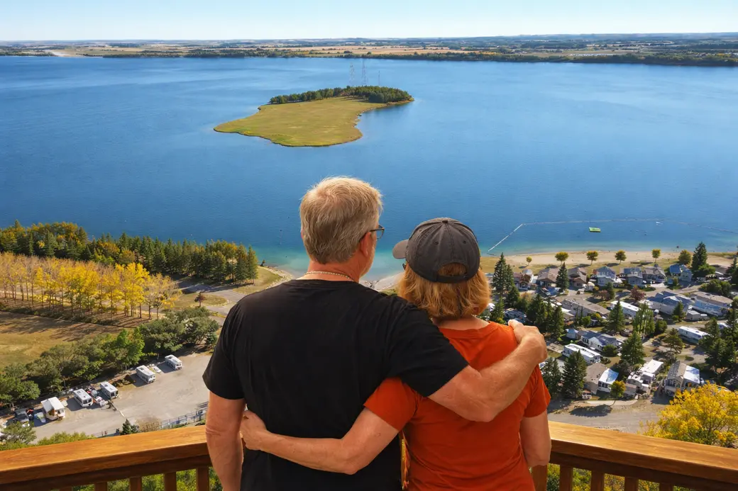 Peaceful Central Alberta lake shoreline with trees and calm water reflecting a recreational lake community lifestyle.
