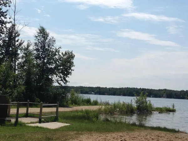 View of Gull Lake shoreline in Central Alberta with sandy beach, lakeside trees and calm water showing the relaxed recreational lifestyle at Gull Lake.
