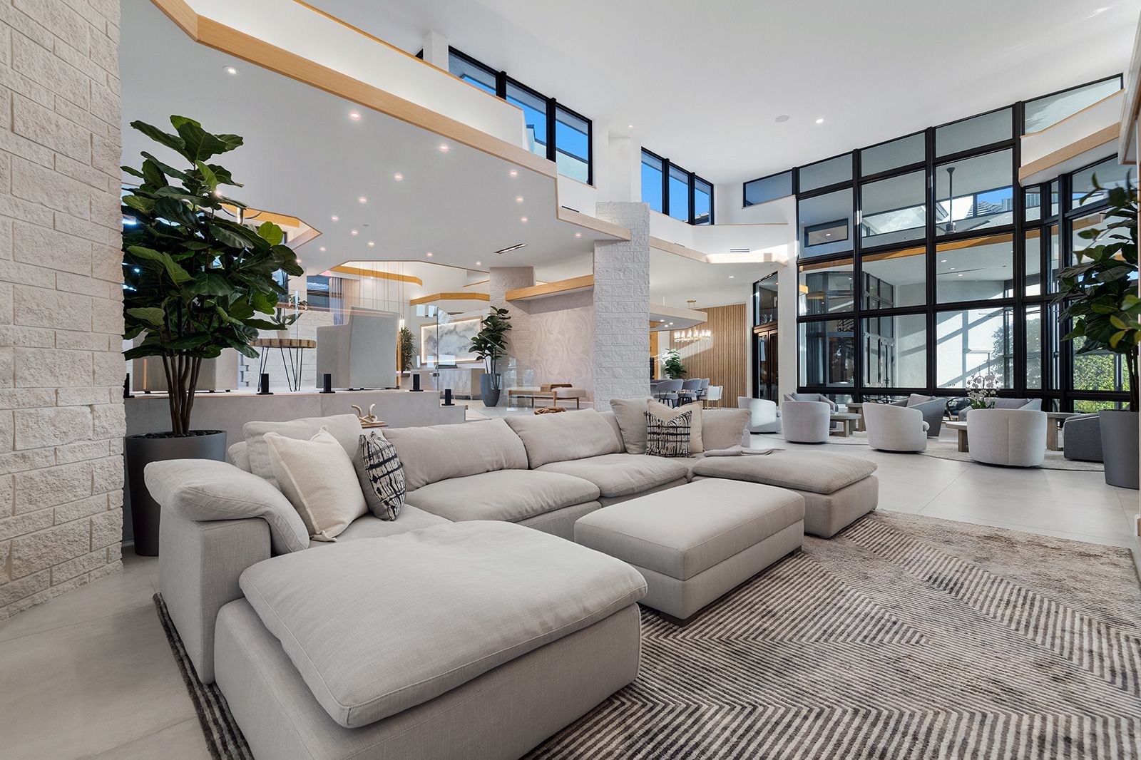 Double height great room with a light sectional, black steel glass wall, and white stone columns in a Weston, Florida luxury home