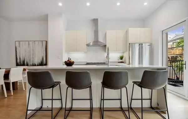 Wicker Park new-construction kitchen with waterfall island, four barstools, white cabinets, stainless appliances, and patio access.