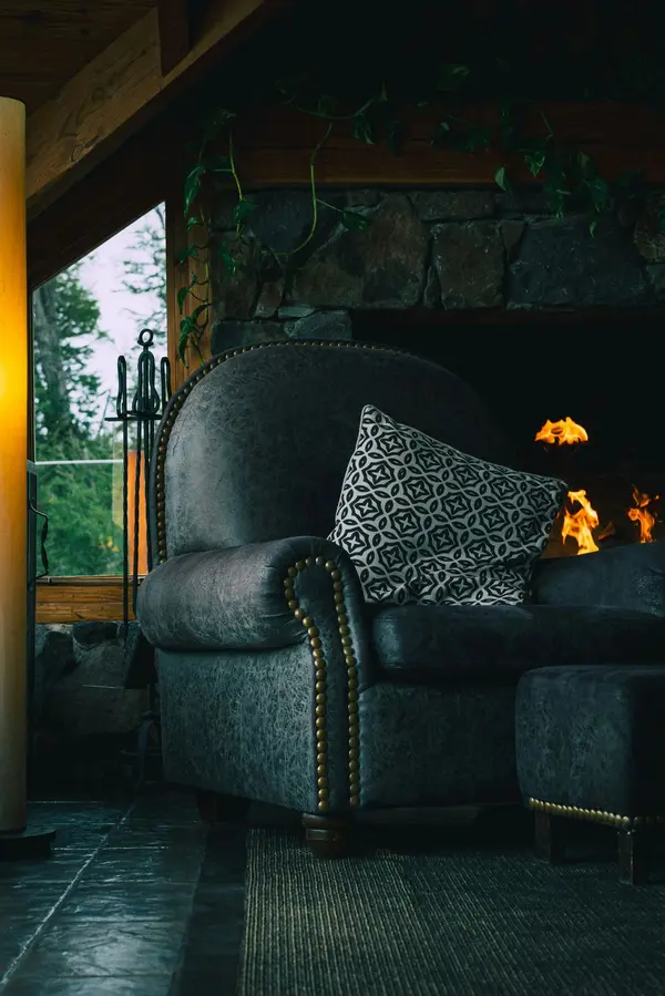 Over stuffed chair in cozy cabin with fire in the fireplace.