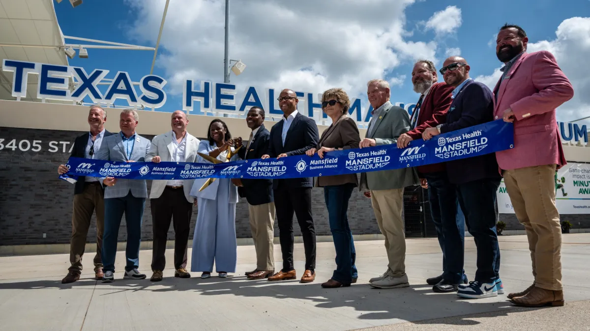 Community leaders and project developers pose with a ceremonial ribbon and scissors to commemorate the opening of Texas Health Mansfield Stadium July 1, 2026, in Mansfield. (Joseph Morgan | Fort Worth Report)