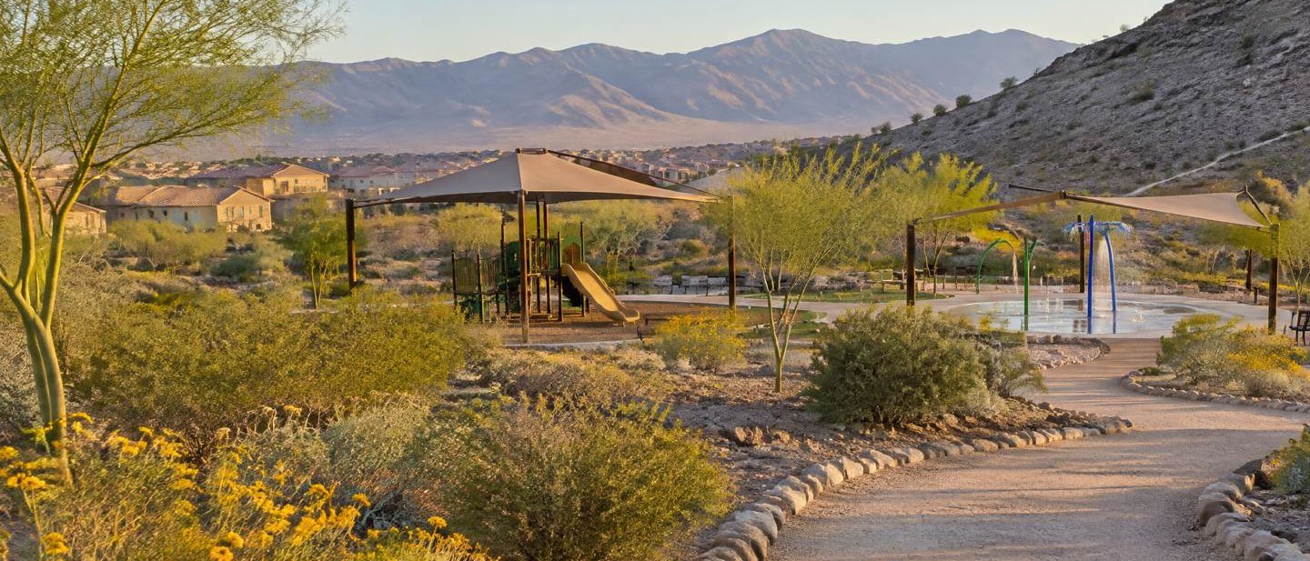 Illustration of tile-roof homes beside a shaded playground and splash pad, with mountains behind.