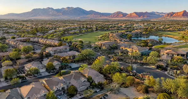 Aerial view of stucco, tile-roof neighborhoods and a gated golf area with mountains beyond in Spring Valley, Las Vegas