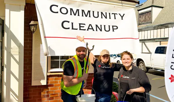 Community Event - Cleanup - group of smiling people holding cleanup supplies in front of a brick building with a "community cleanup" sign above them