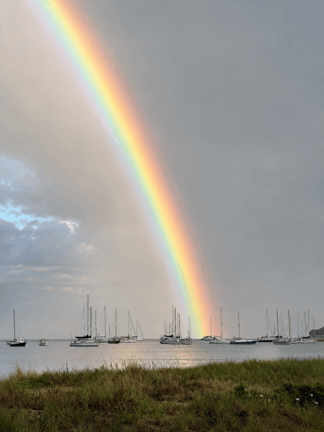 Vivid rainbow band over moored sailboats in Padanaram Harbor