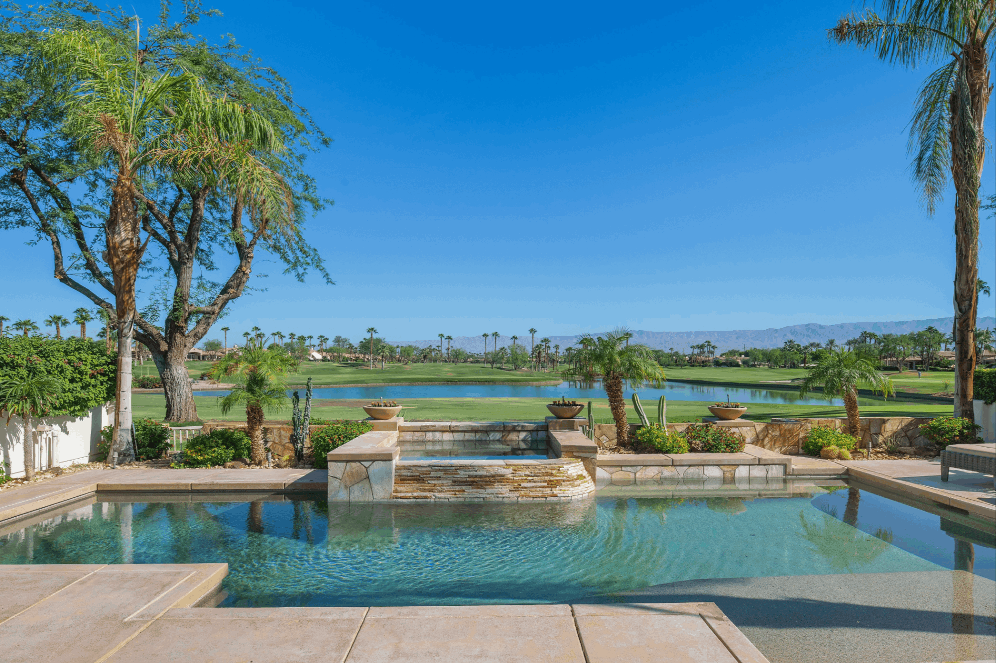 Private pool at a Rancho La Quinta residence overlooking a lake, golf course fairways, palm trees and desert mountains