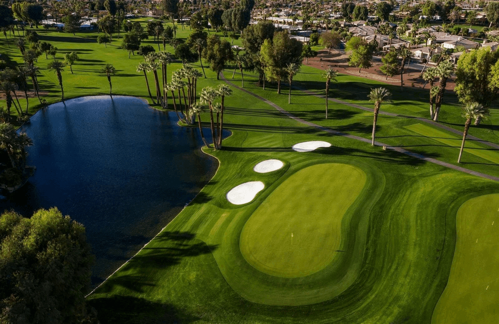 Aerial view of Bermuda Dunes Country Club featuring golf course fairways, lake, mature trees and surrounding residences in Bermuda Dunes, California