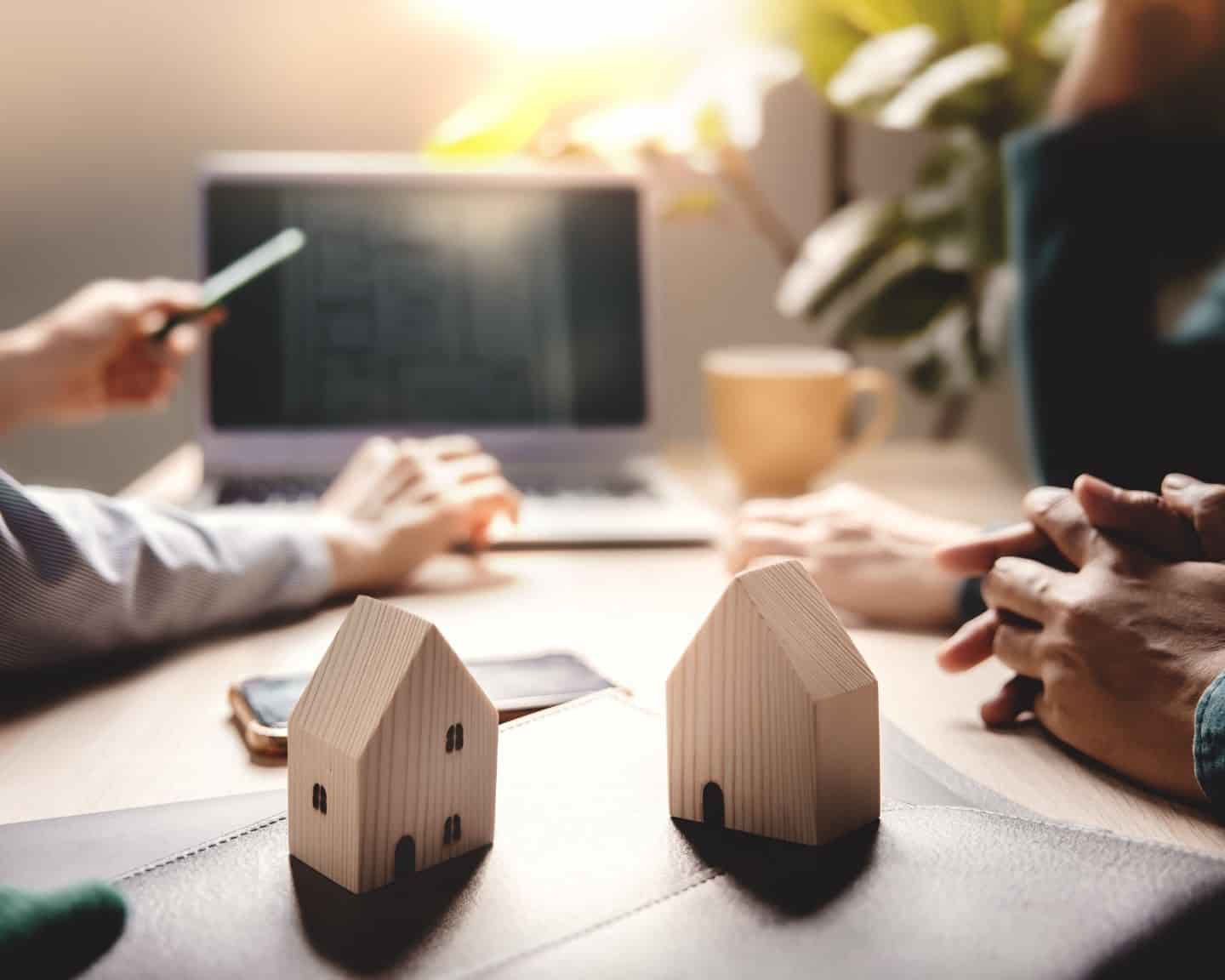 Home buyers meeting with a real estate agent, reviewing property plans on a laptop with small wooden house models on the table, symbolizing the role of a buyer’s agent in Kentucky.