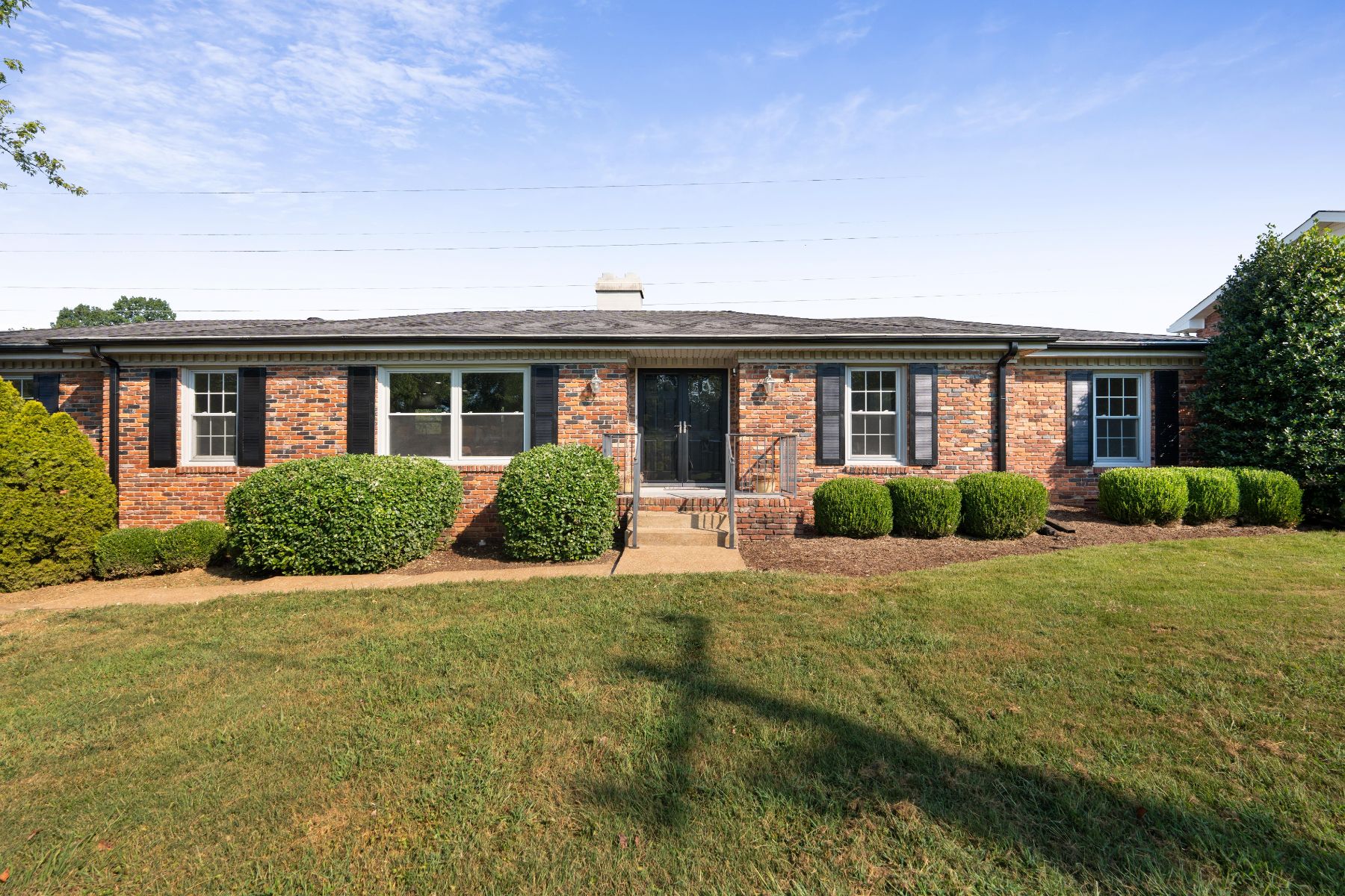 Brick ranch home with black shutters and a green lawn