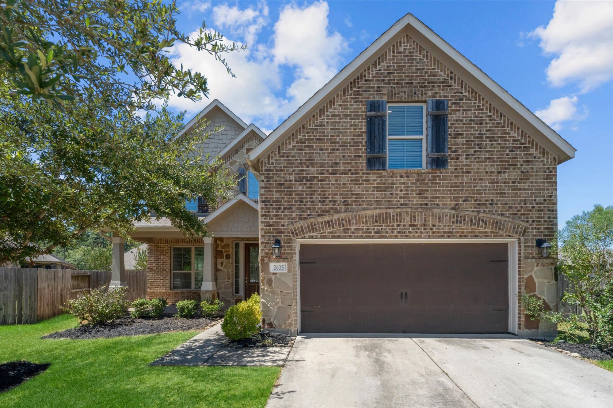 2635 Forest Cove Court in The Meadows at Imperial Oaks in Conroe, TX features a beautifully maintained two-story brick home with stone accents, decorative shutters, mature landscaping, a spacious front yard, and an attached two-car garage