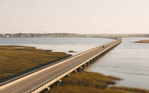 Causeway bridge crossing a wide tidal marsh toward a Northeast Florida coastal town at sunrise