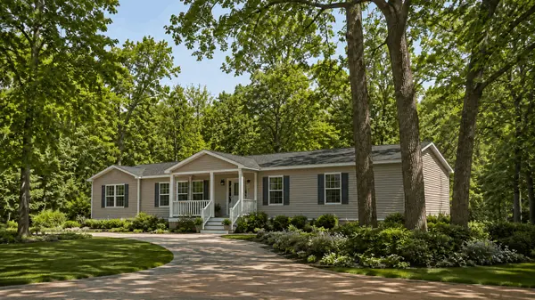 Well-kept manufactured home surrounded by mature trees, lush landscaping, and a curved driveway in a peaceful wooded setting.
