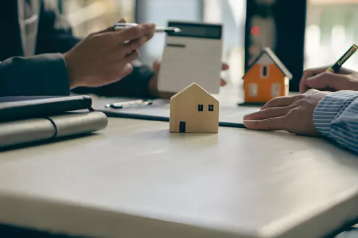 Real estate agents meeting with a client to discuss property sales and investment plans, with small house models on the table.