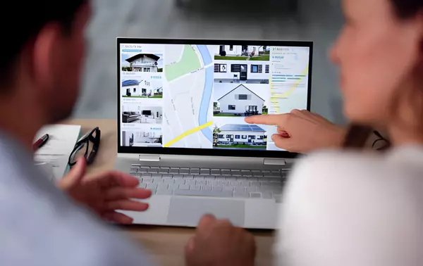 Real estate agents reviewing online property listings and neighborhood maps on a laptop, discussing homes for sale and location details.