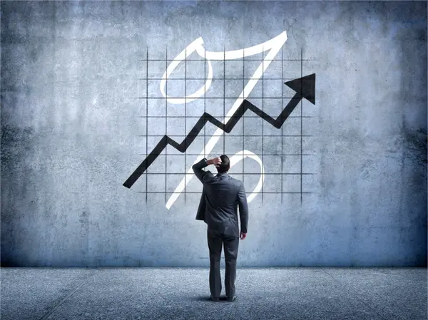 A businessman in a suit stands before a wall displaying an upward trending arrow and financial growth chart