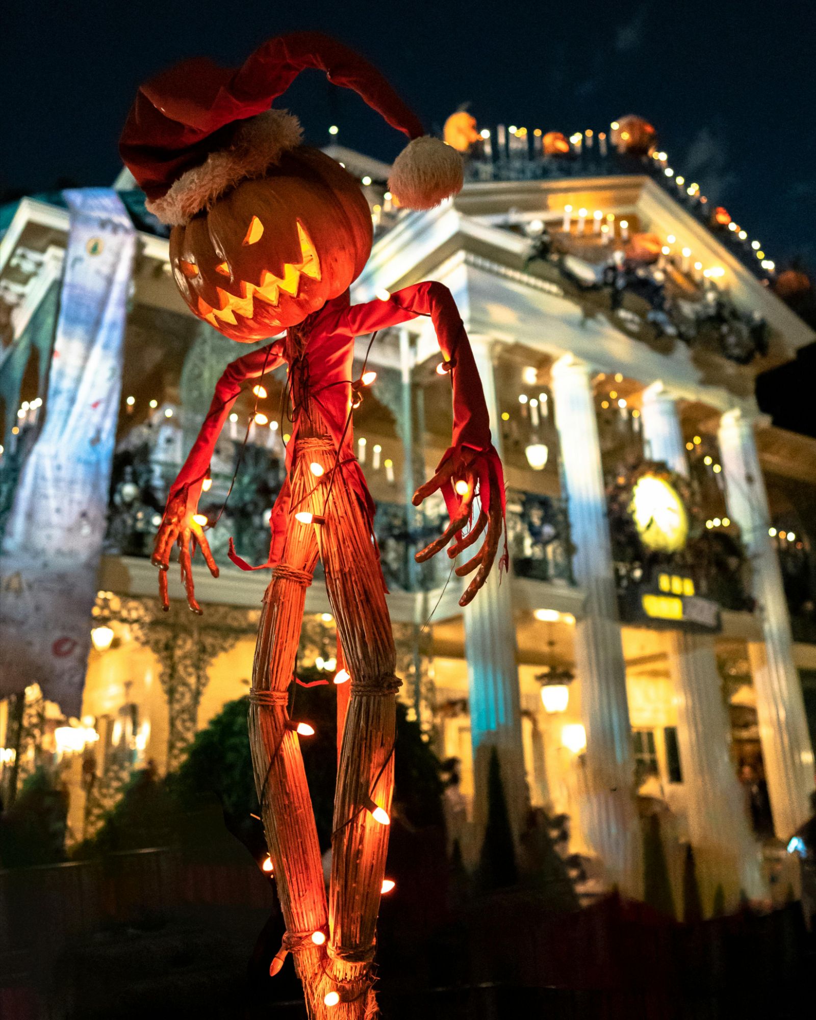 House and front yard decorated for Halloween with glowing jack-o’-lanterns and props at night