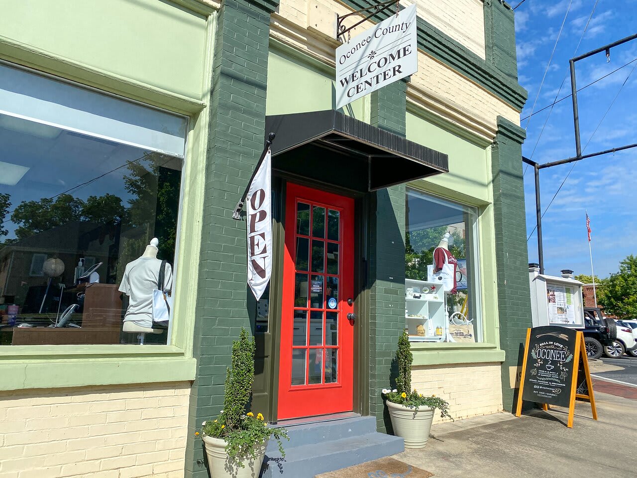 The welcoming storefront of Oconee County Welcome Center located in downtown Watkinsville, Georgia, with its distinctive green brick and red door entrance, serving as a resource for veterans and community members throughout greater Athens.