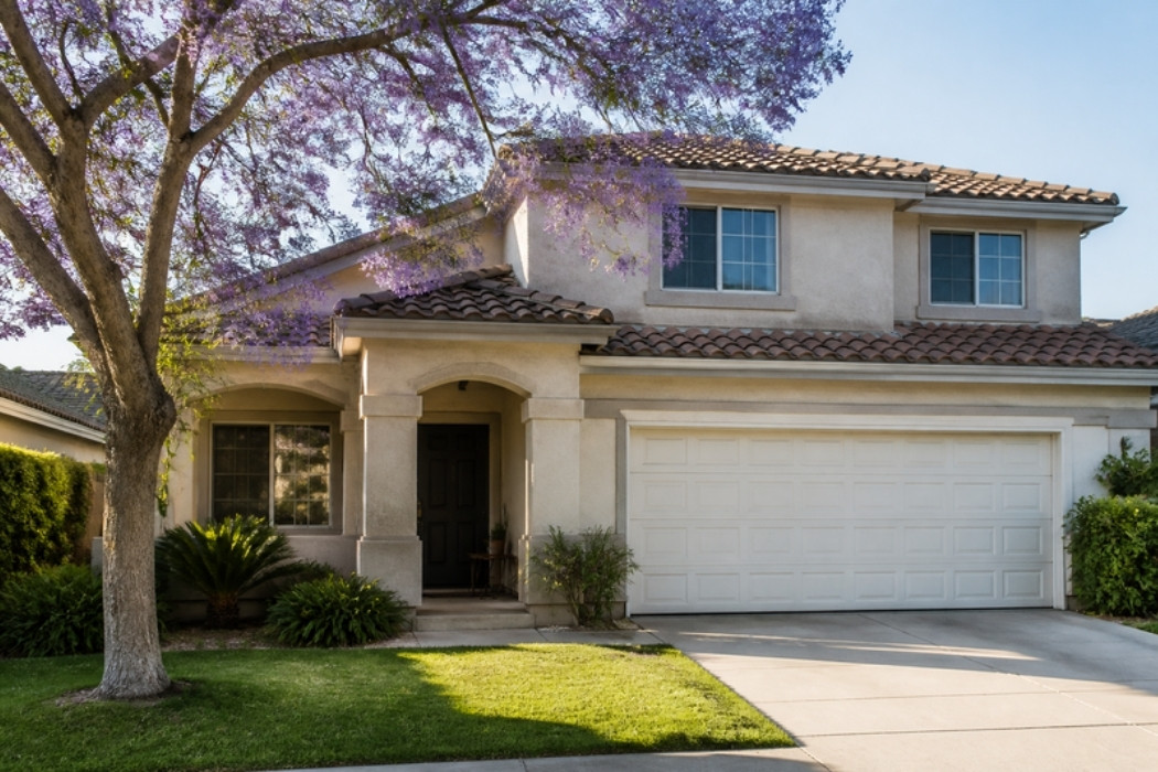 Two story stucco Southern California home with a blooming jacaranda tree and a neat front lawn