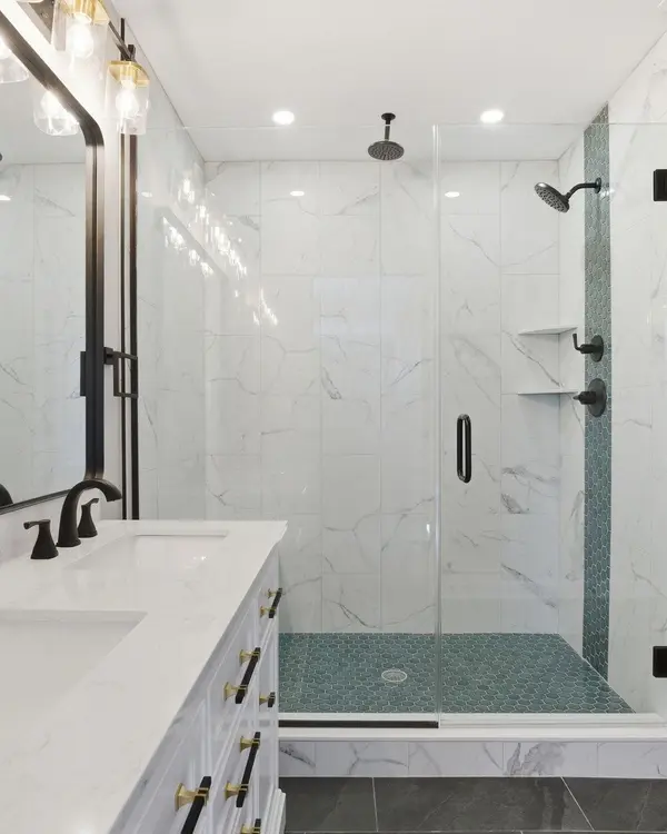 Remodeled bathroom with a glass-enclosed tile shower, green hexagon tile floor, and white double vanity