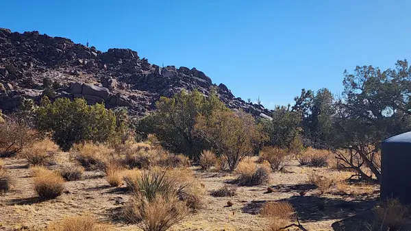 Image of desert property with water tank and boulder in mountain backdrop