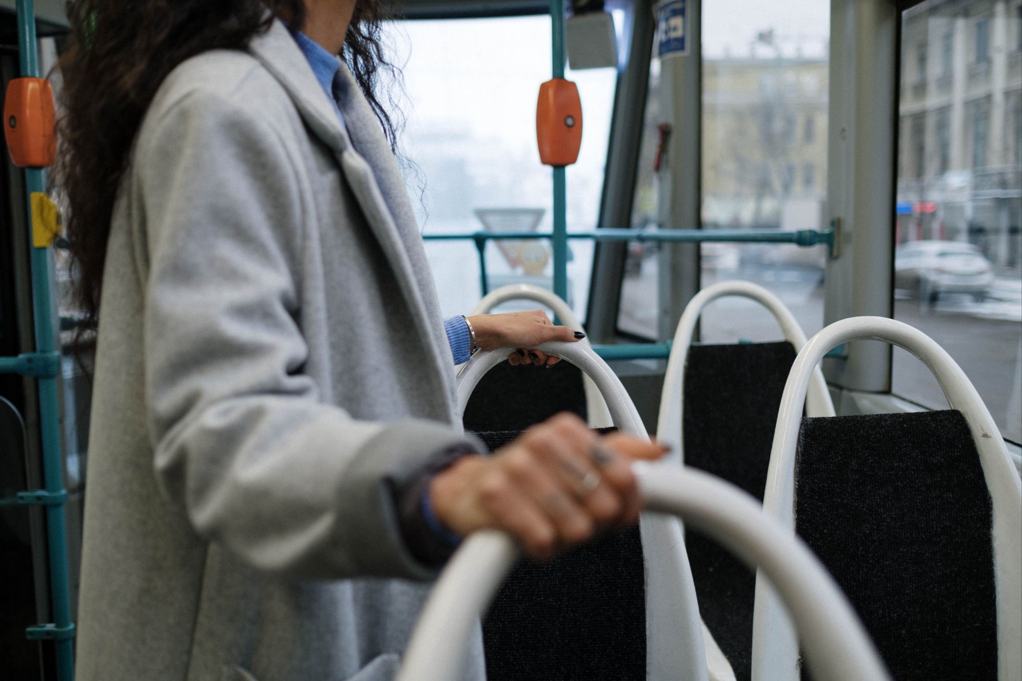Close-up of a commuter wearing a grey coat holding onto the white handrails inside a city public transit bus