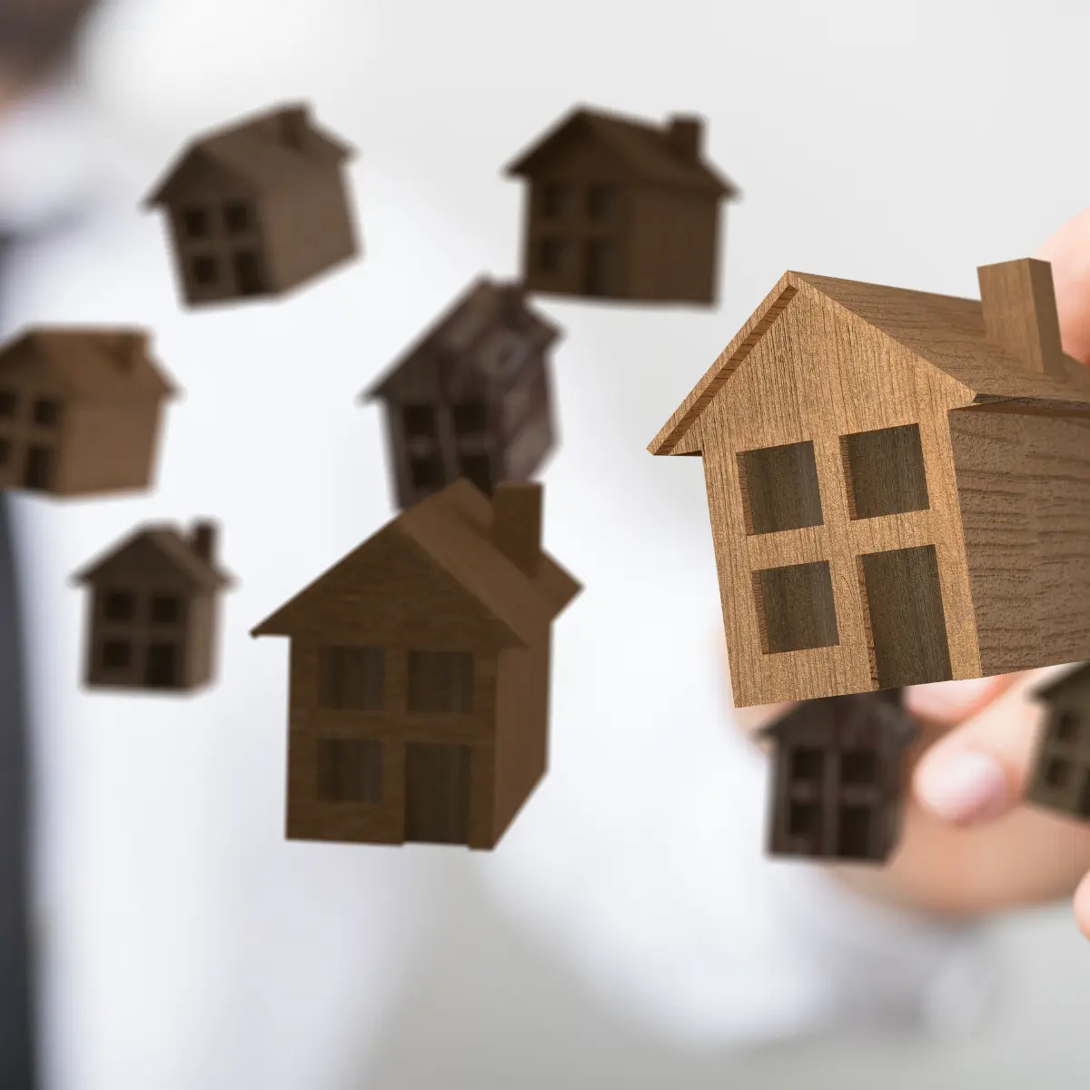 Portland real estate agent hand holding small wooden house models, representing relocation to or from Portland