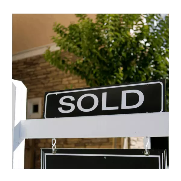 Close-up view of a black and white SOLD real estate sign hanging from a white post outdoors representing the successful home sale.