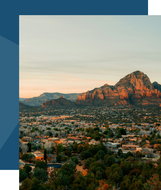 Landscape photo: a desert town with red rock mountains in the background, residential area and trees in foreground, vertical orientation showing sky and terrain.