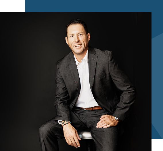 Portrait of a male realtor sitting on a stool, three-quarter length, dark studio background, wearing a suit