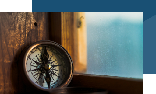 brass compass resting on a wooden windowsill with a soft blue out-of-focus window background, landscape aspect ratio