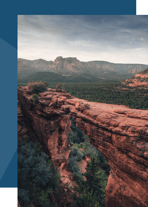 Scenic canyon view with red rock natural bridge arching above a forested valley, tall portrait photograph