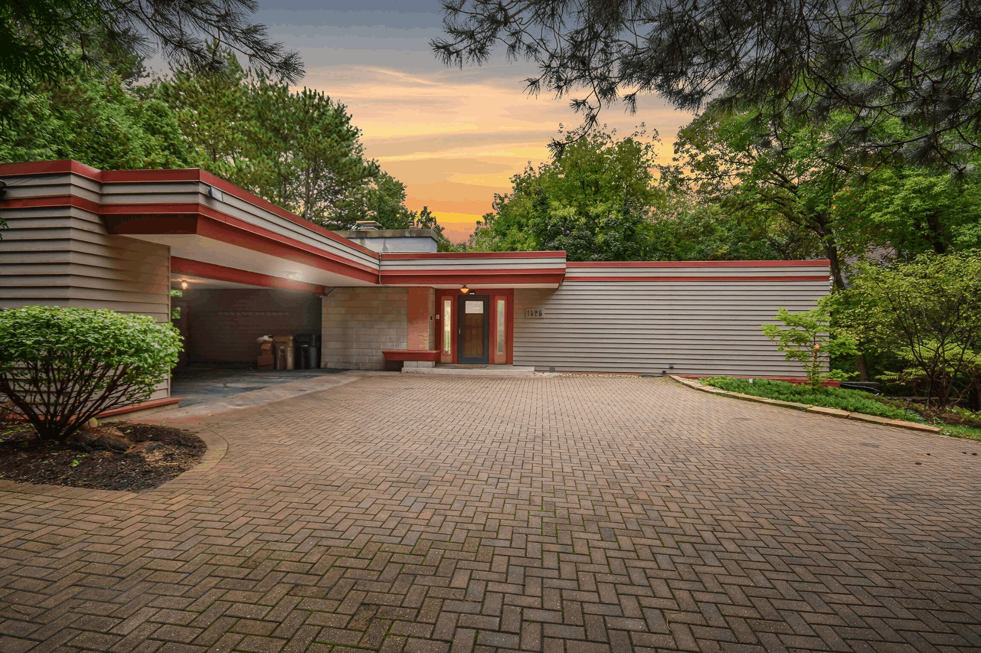 Photo of a brick-paved driveway framed by trees and homes, landscape orientation