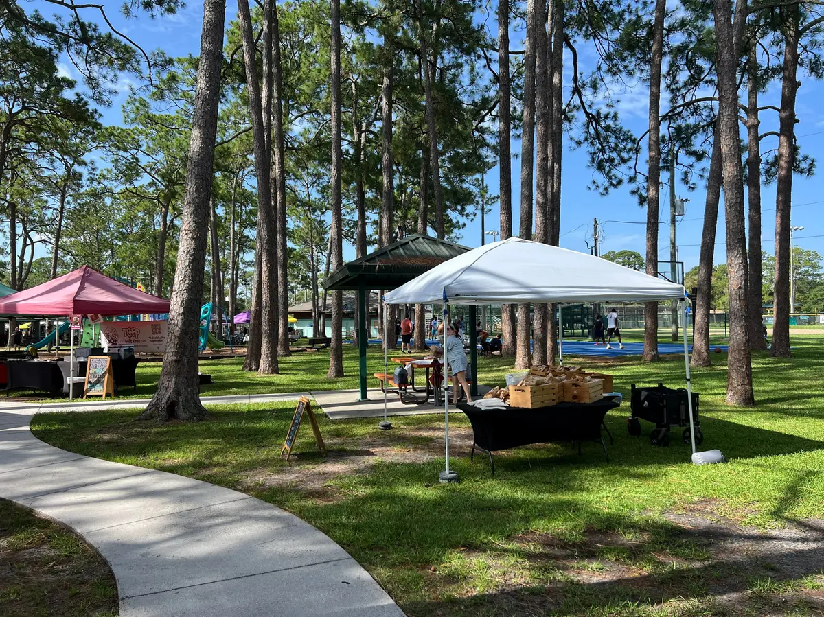 Community event in a wooded Atlantic Beach park with vendor tents, recreation areas and local gathering spaces.