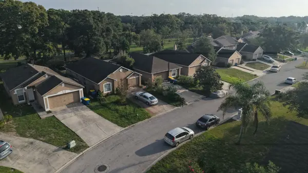 Aerial view of homes with attached garages, lawns and mature trees along a residential street.