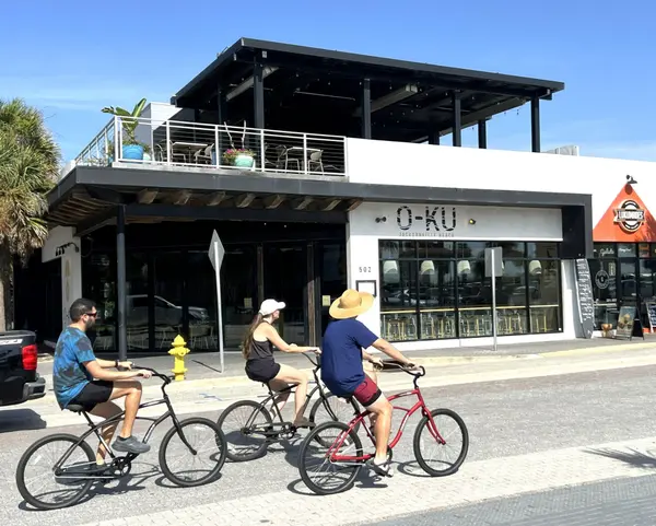 People riding bicycles past local restaurants in Jacksonville Beach, Florida, highlighting the community's walkable streets, outdoor dining, and active coastal lifestyle.